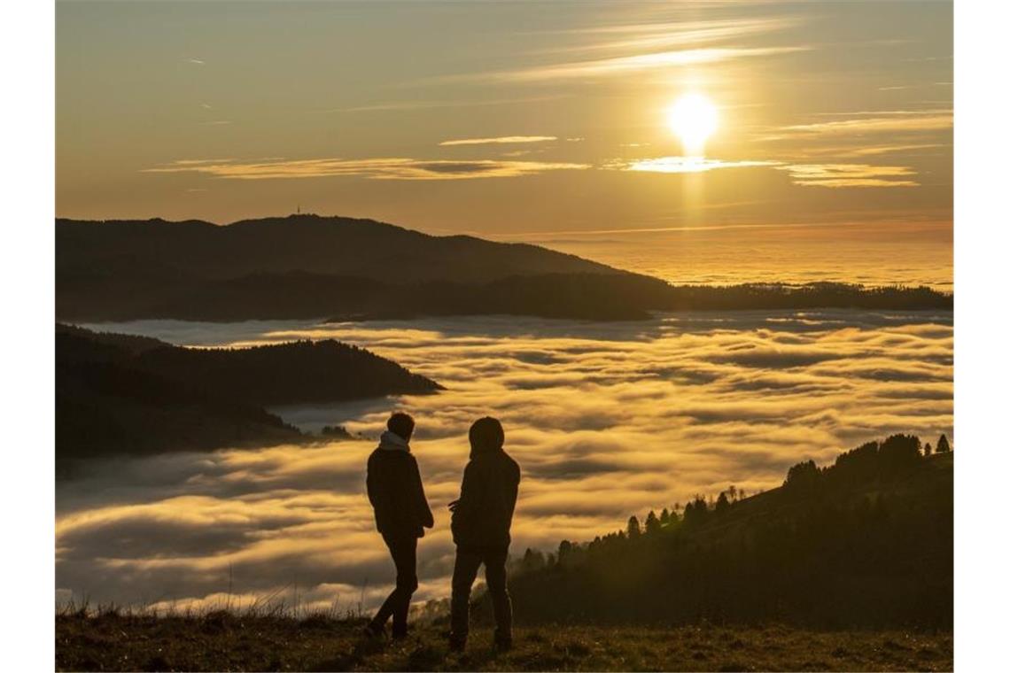 Zwei Spaziergänger betrachten den Sonnenuntergang über dem Wolkenmeer. Foto: Patrick Seeger/dpa/Archivbild